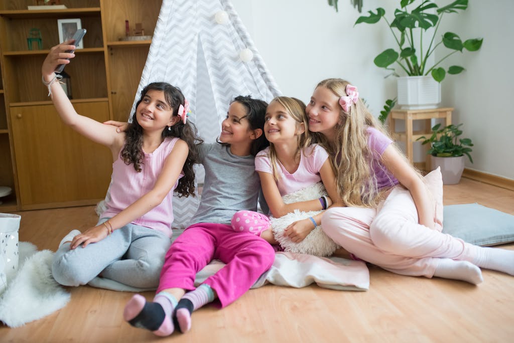 Four smiling girls take a fun selfie indoors, enjoying quality time together at home.