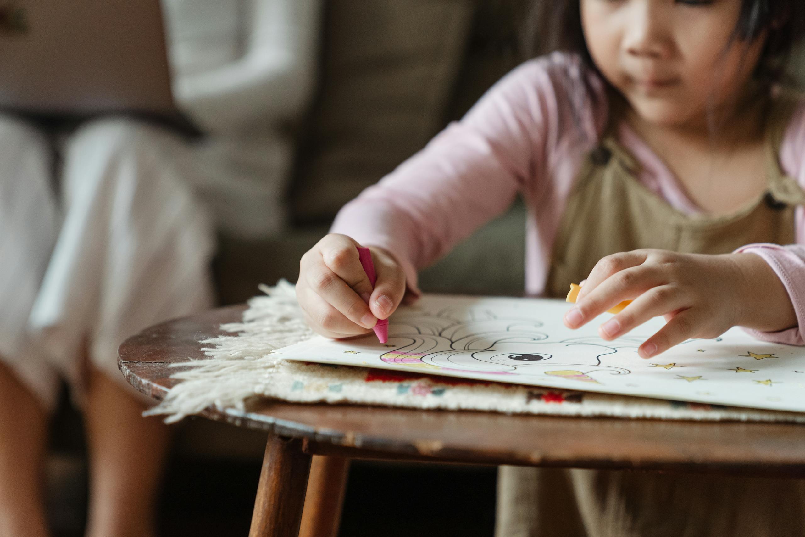 A child focuses on drawing while a parent works on a laptop in a cozy home environment.
