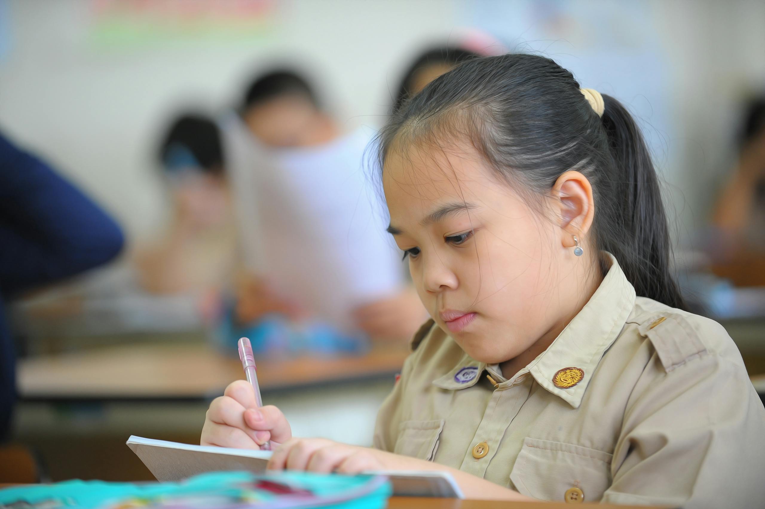 Asian girl diligently writing in a notebook during class in a school setting.
