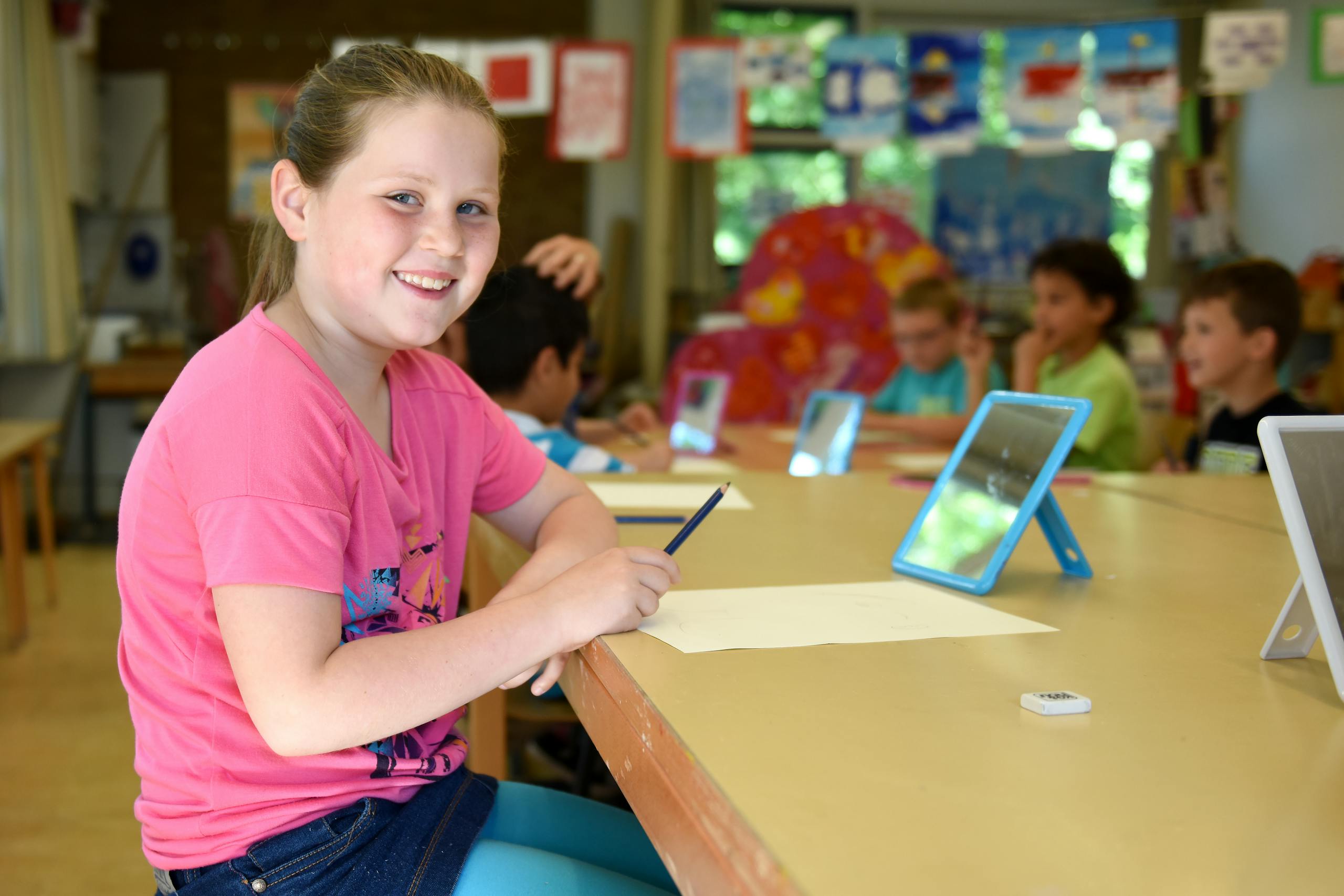 Smiling girl in a bright classroom during a lesson with classmates engaging in learning activities.