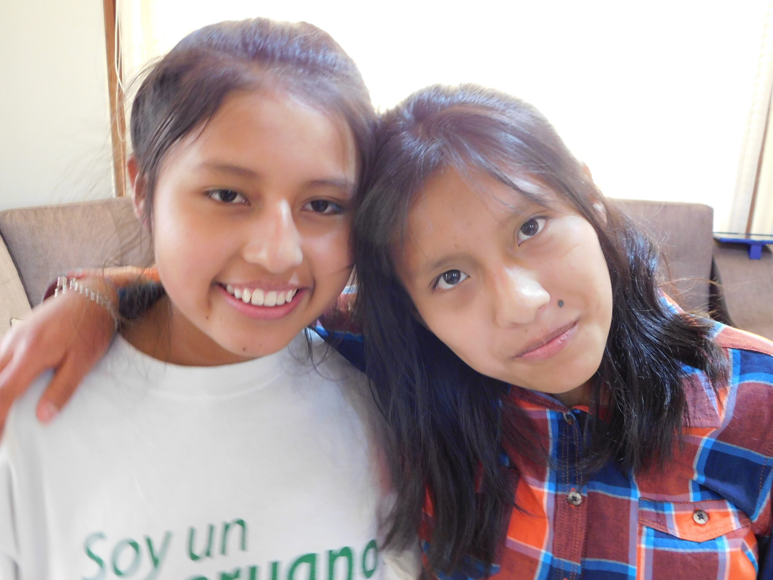 Four smiling girls take a fun selfie indoors, enjoying quality time together at home.